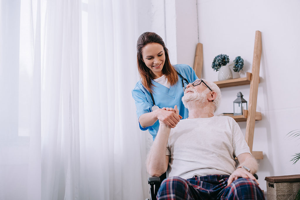 Nurse supporting and holding hand of smiling senior man patient
