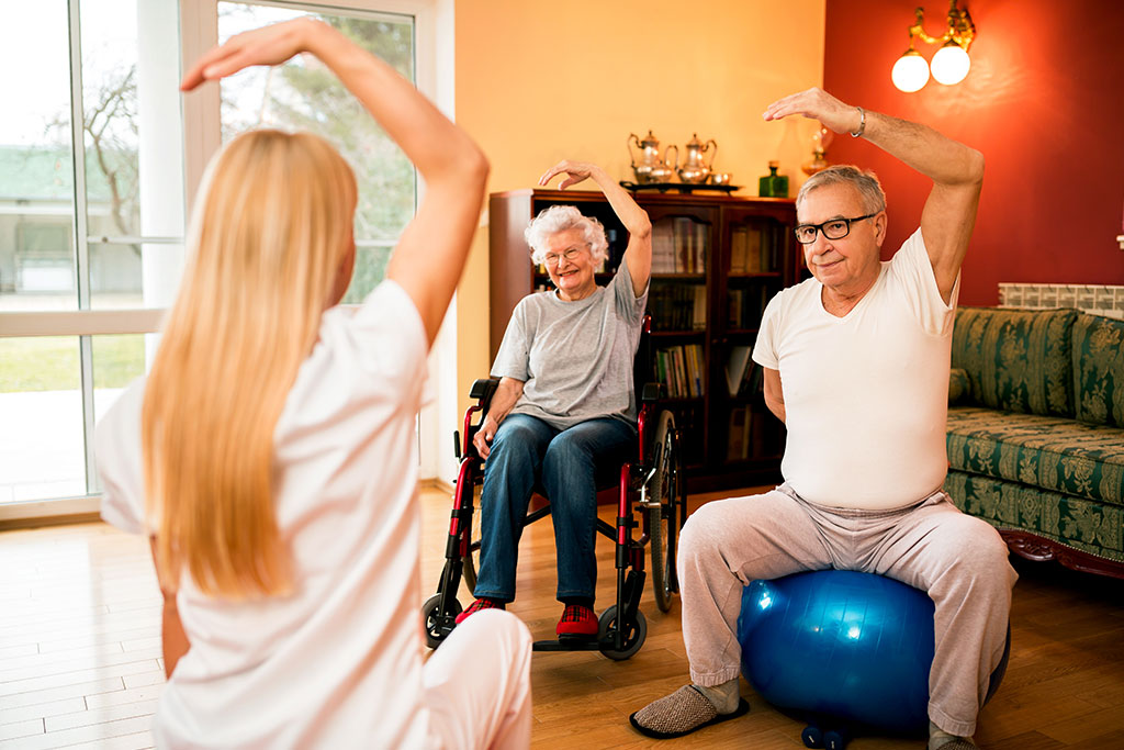 Physiotherapist shows exercise to senior couple, healthcare concept