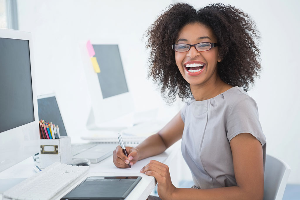 Young pretty designer smiling at camera at her desk